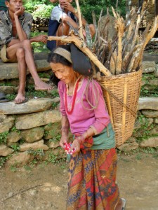尼泊爾︰圖中年過五旬的婦女，剛從山上砍柴回來。她揹著柴枝，從兩個悠閒地坐在樹下納涼的男村民旁邊走過。她身上的重擔跟其纖瘦的身子形成了對比。