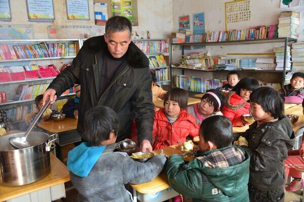 這位在分發午餐給同學的是罐峽小學的校長劉凱軍，由於老師人手不足的關係，所以校長除了管理學校以外，也會負責教學和一些雜務。