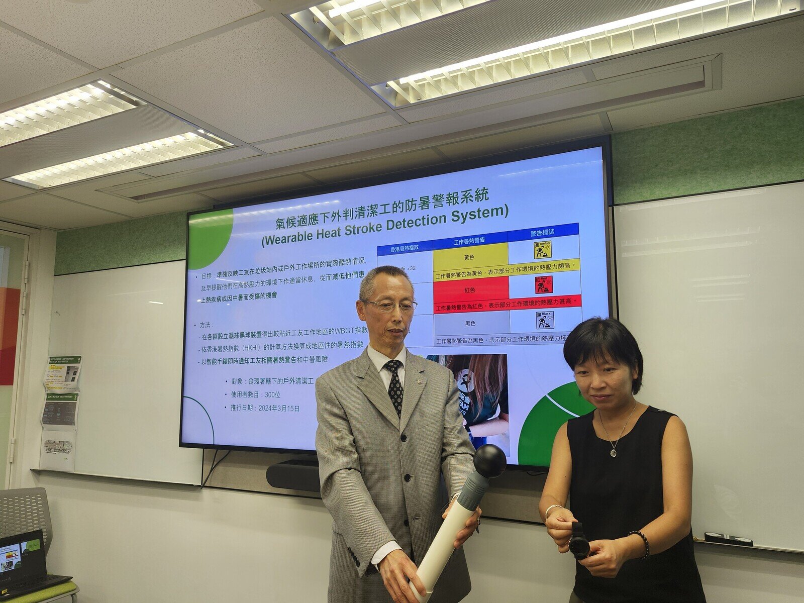 Mr. Ricky Law, Director, LinkAIQ Limited, Cyberport and City University of Hong Kong's HK Tech 300 Start-up and Ms. Wong Shek Hung, Director, Hong Kong, Macau and Taiwan Programme demonstrate the wet bulb globe temperature (WBGT) device and smart heat bracelet.