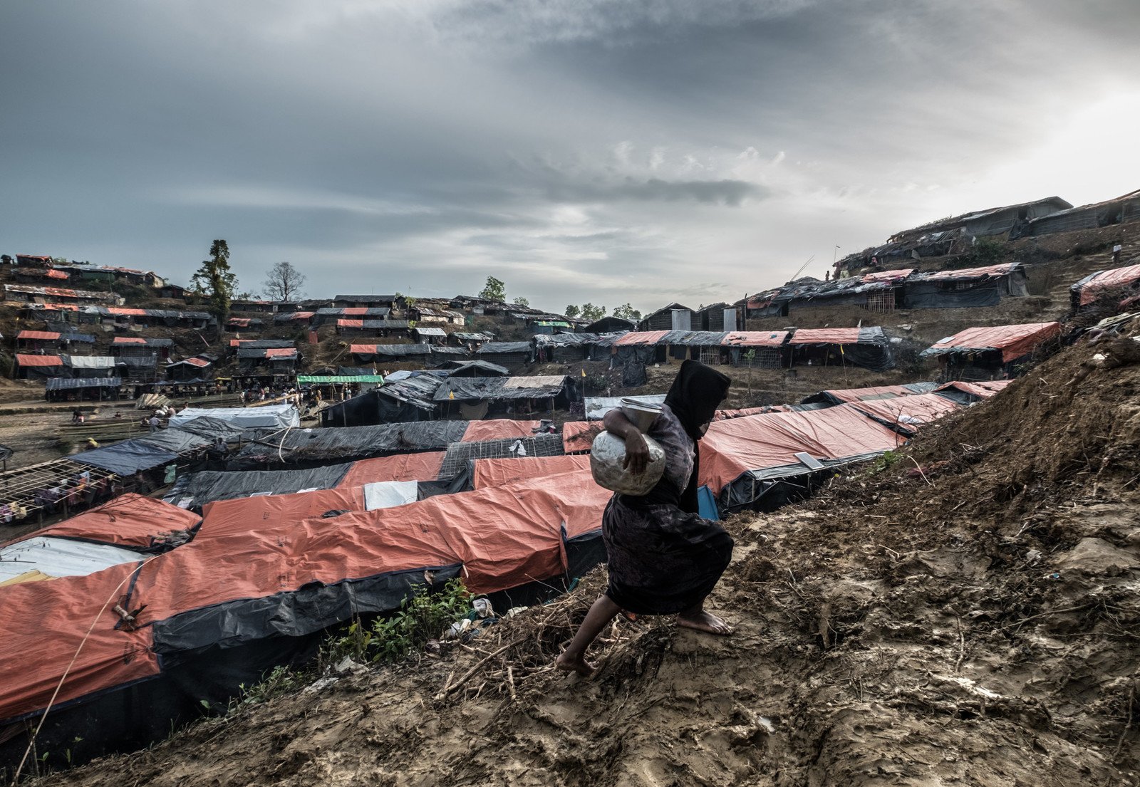 A woman carries a jar of water up a muddy slope in Balukhali camp, where thousands of Rohingyas are now living. photo: Tommy Trenchard/Panos