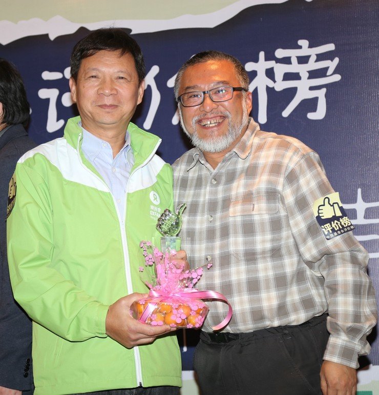 樂施會中國項目總監廖洪濤從頒獎嘉賓手中接過金桔獎獎盃和象徵性獎品一盒桔子。