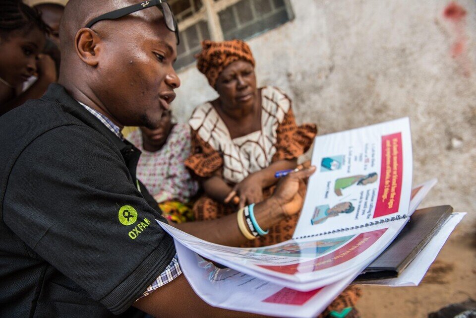 Photo: Tommy Trenchard / Oxfam Abdul Razak Baimba, A Community Health Worker talks with residents of Congo Town in Freetown (Sierra Leone) about Ebola. Oxfam has provided handwashing stands in the area and have also trained Community Health Worker teams who teach the community about the signs and symptoms of Ebola, how to prevent it and what to do if a family member becomes infected.