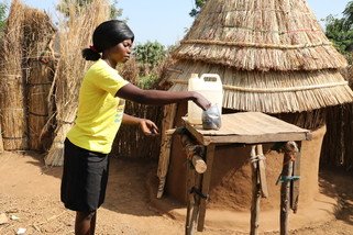 Woman washing hands in front of a hut