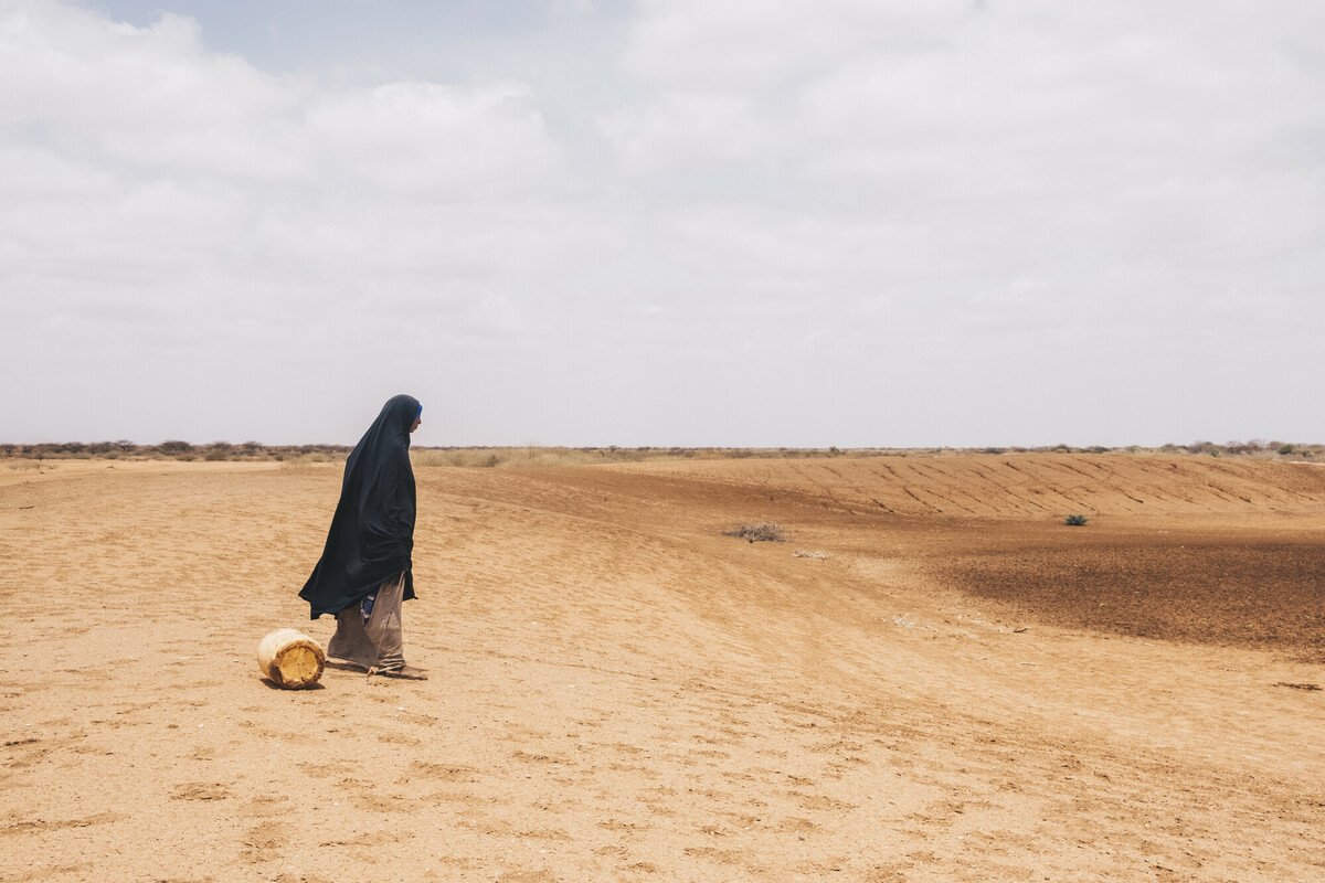 Woman walking toward an empty water hole with a jerican.
