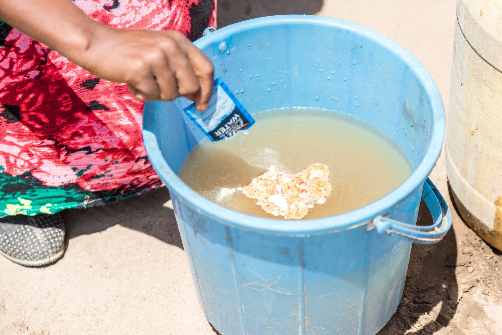 Water purifying powder being poured into a bucket of dirty water.