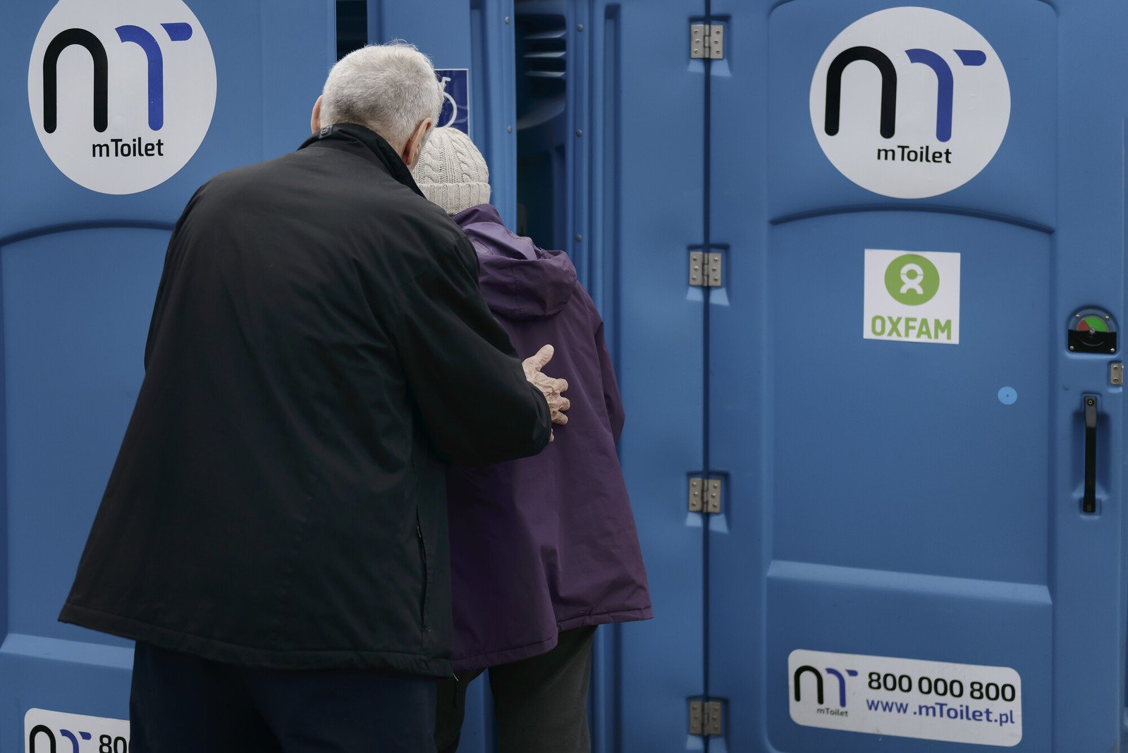 An elderly man and woman walking together towards Oxfam's portable toilets.