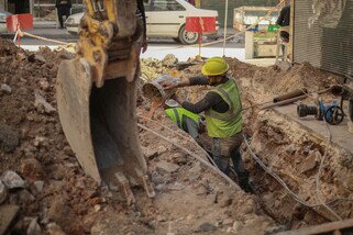 Two Oxfam staff in a ditch with an excavator beside them.