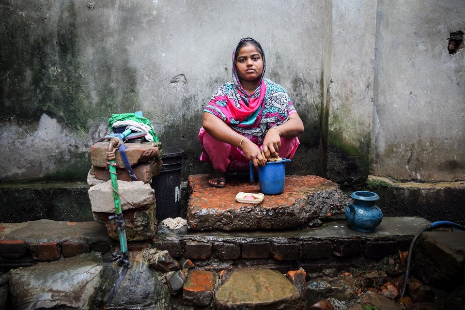 A woman from Bangladesh doing her laundry by an open sewer.
