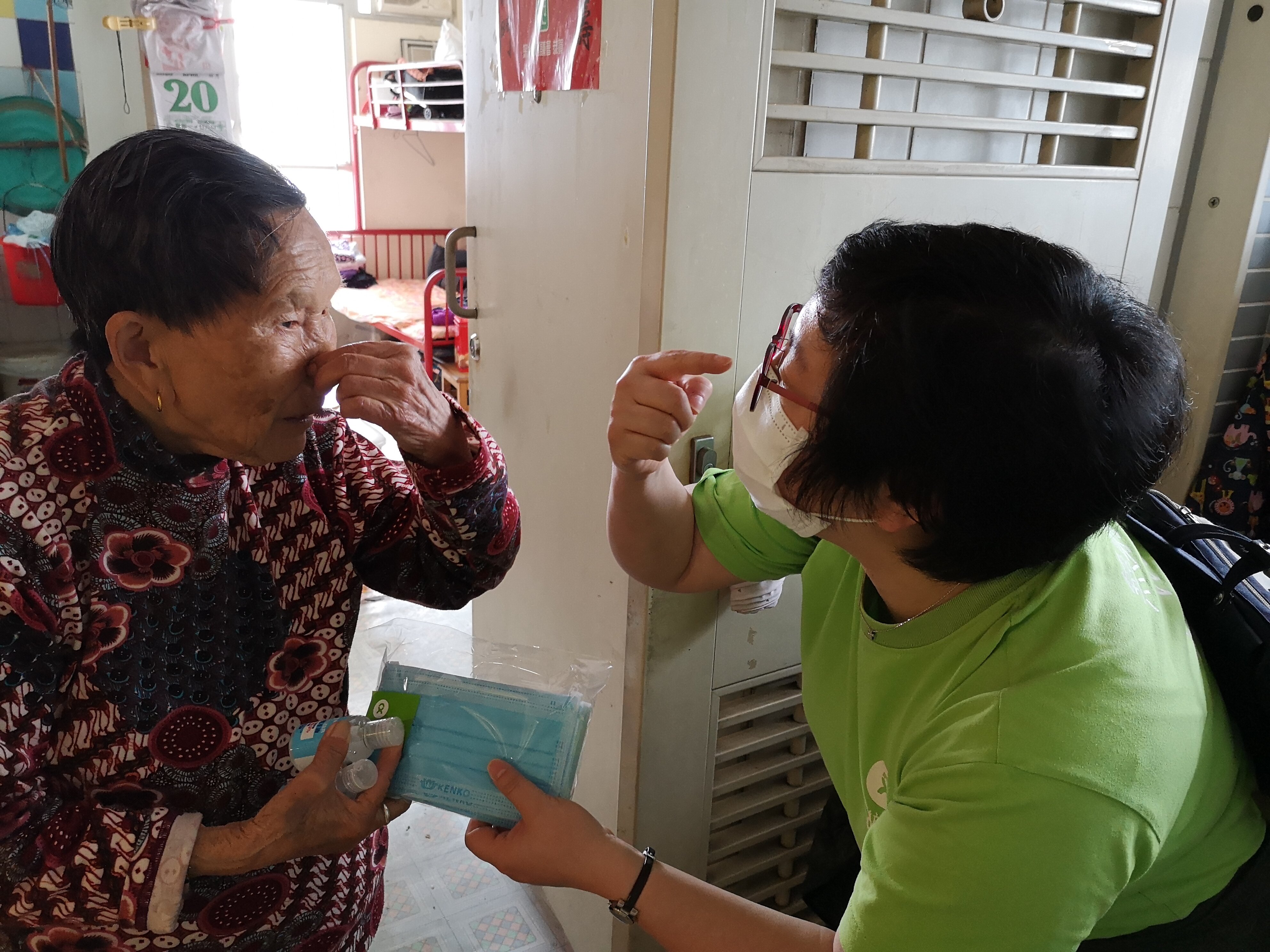 Oxfam staff member showing a senior how to put on a mask properly