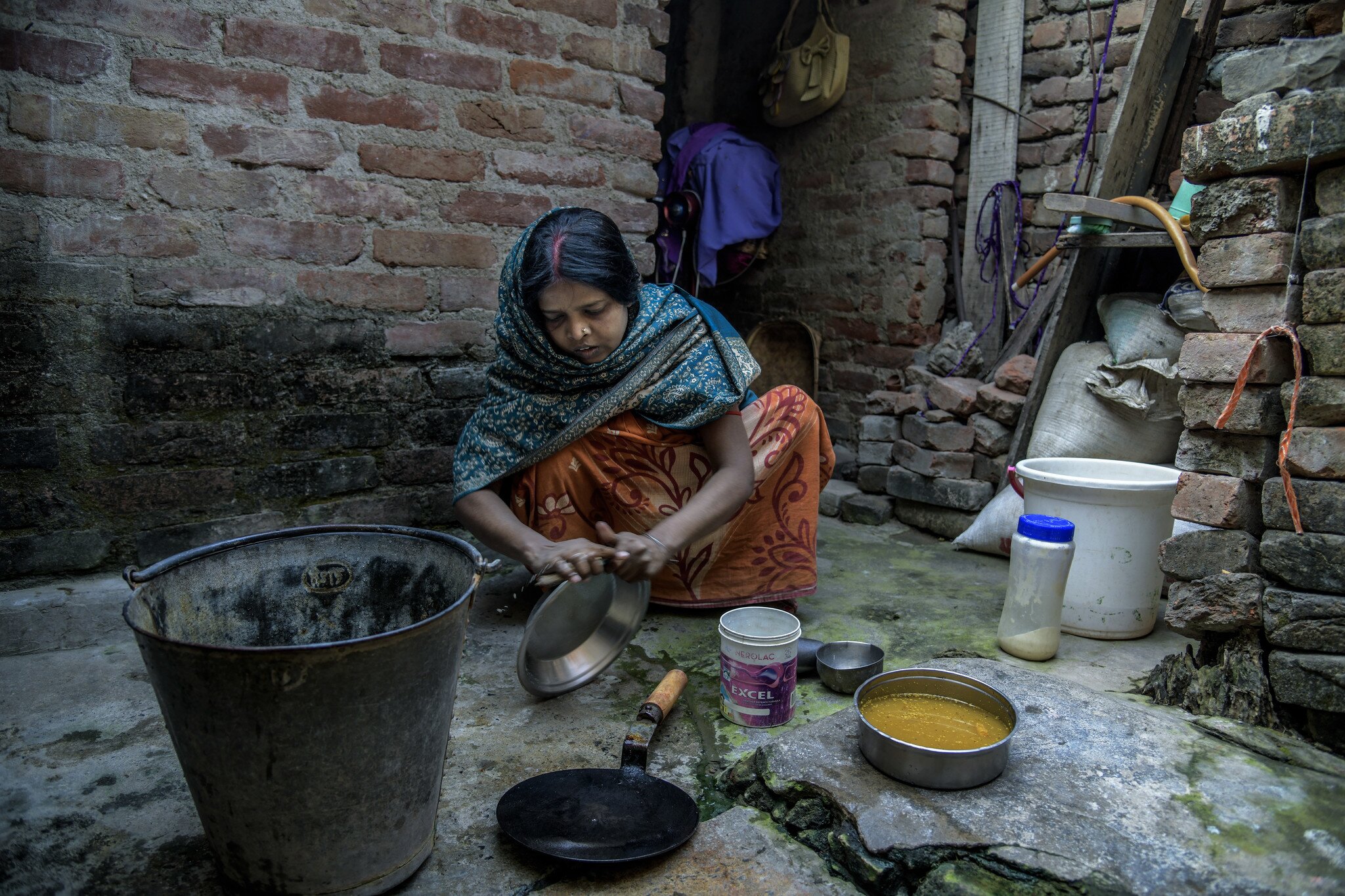 Indian woman squatting and washing her pots and pans in a rundown place.