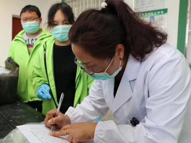 Health worker writing. Oxfam staff standing beside her.